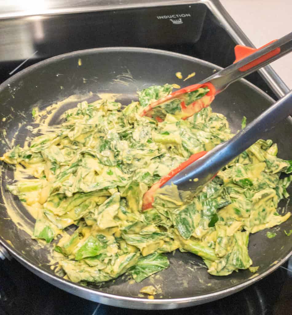 collard greens cooked down in pan with tongs after stirred with cheeze sauce