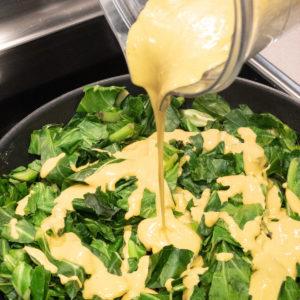pouring cheeze sauce over collard greens in pan