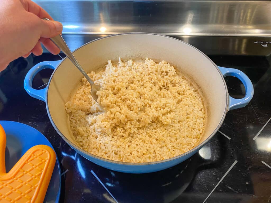 fluffing rice in a pot on the stove with a fork.
