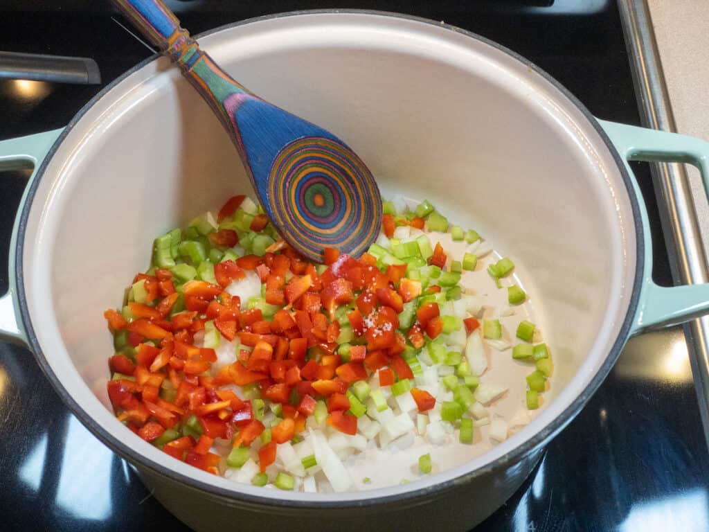 diced yellow onion, celery, and red pepper in pot with colorful spoon