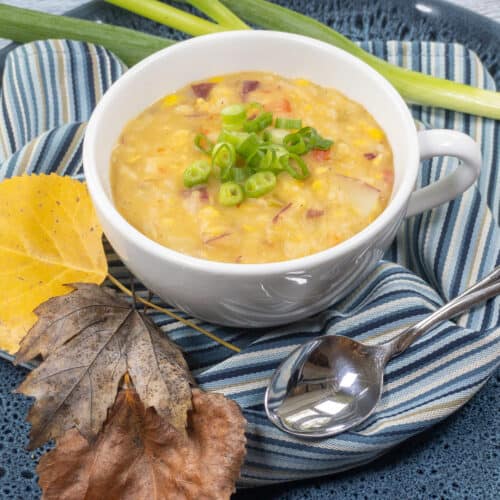 Sweet Corn Chowder in white mug over blue striped linen with spoon and leaves