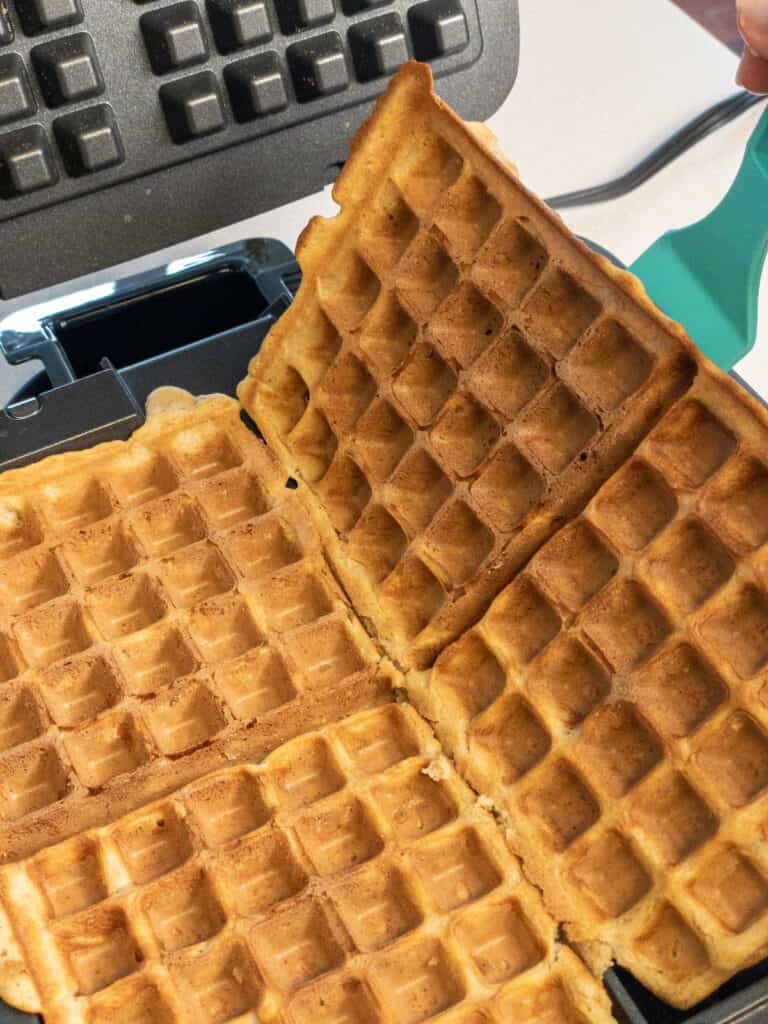 Easily lifting two of the four cooked waffles out of the waffle maker with a spatula
